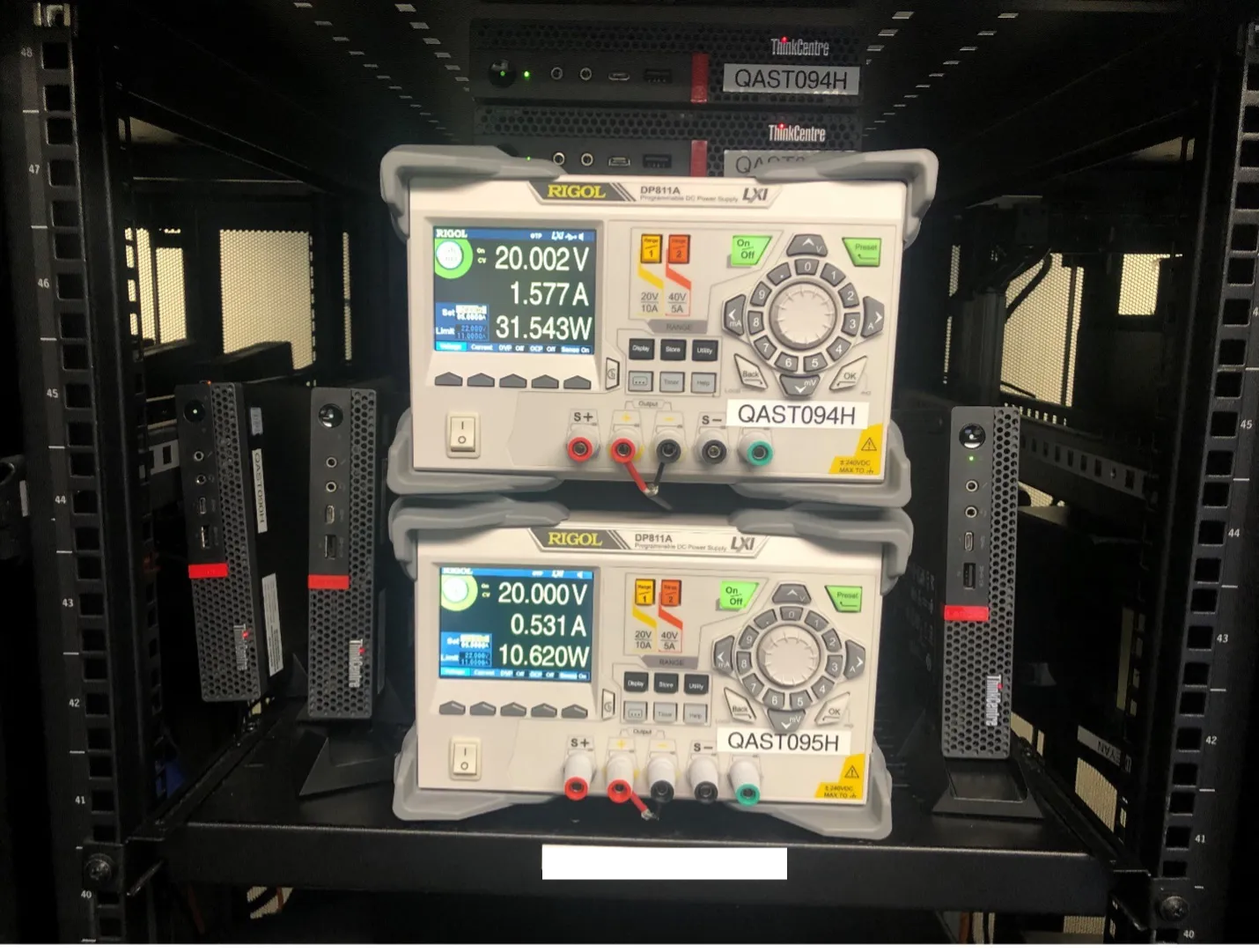 Two Rigol benchtop power supplies mounted in a server rack displaying voltage, current, and power readings